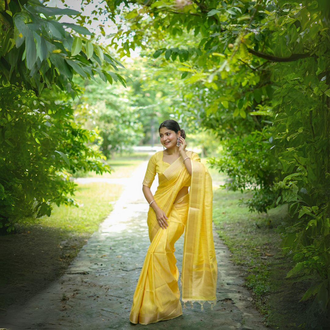 Woman in yellow zari work saree standing in a lush green park with trees in the background